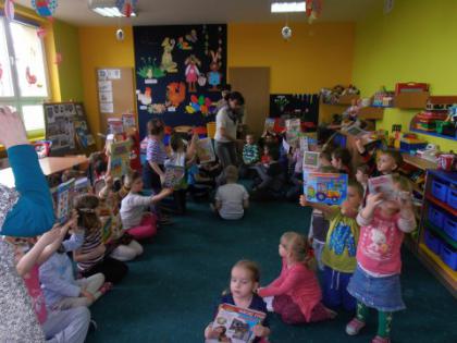 Przedszkolaki siedzą na dywanie i oglądają książeczki.