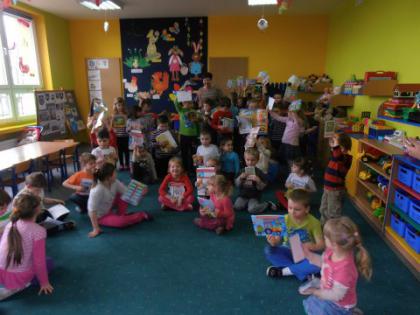 Przedszkolaki siedzą na dywanie i oglądają książeczki.