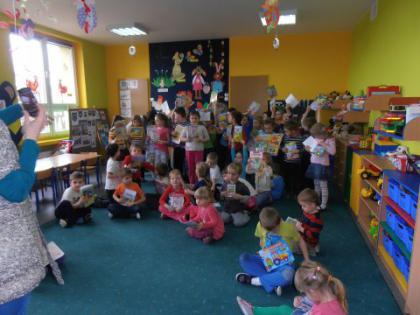 Przedszkolaki siedzą na dywanie i oglądają książeczki.