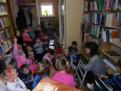 Przedszkolaki słuchają bajeczki czytanej przez panią bibliotekarkę.