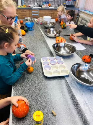 Dzieci na warsztatach wkładają papilotki na muffinki do formy. 