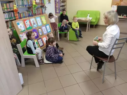 Pani bibliotekarka opowiada dzieciom bajki. Dzieci siedzą i słuchają.