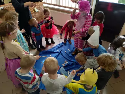 Dzieci na warsztatach w bibliotece łowią papierowe rybki. Dzieci są ubrane w stroje postaci z bajek.