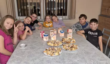 Dzieci siedzą przy stole, na którym są upieczone rogaliki i przy zapalonych lampionach.