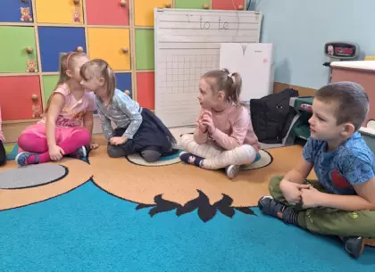 Przedszkolaki bawią się w głuchy telefon na dywanie.