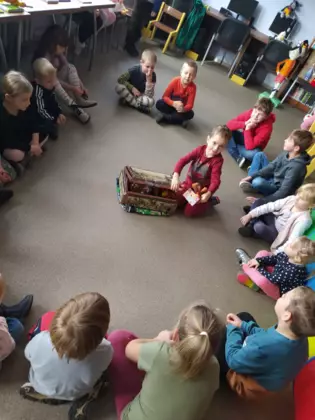 Dzieci siedzą w kole w bibliotece i rozwiązują zagadki.