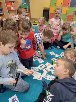 Przedszkolaki bawią się na dywanie w grę sprawdzając bohaterów bajek latarką.