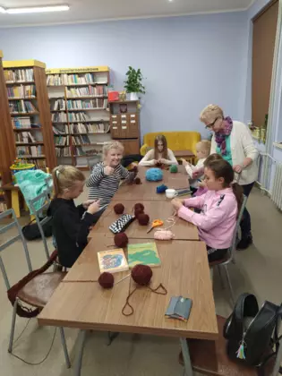 Uczestnicy zajęć siedzą przy stole i szydełkują.