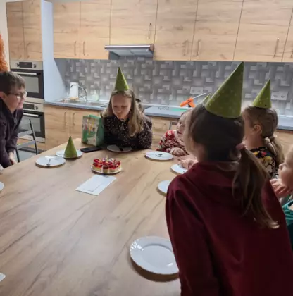 Dzieci siedzą przy stole i świętują urodziny Zuzi.