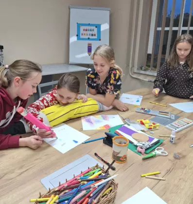 Dziewczyny malują obrazki kolorowymi kredkami.