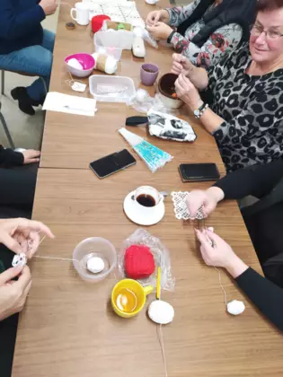 Panie siedzą przy stole i szydełkują.