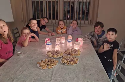 Dzieci siedzą przy stole, na którym są upieczone rogaliki i przy zapalonych lampionach.