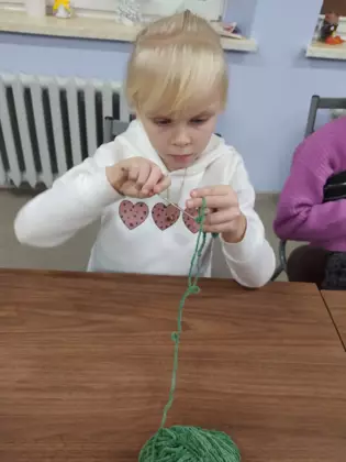 Dziewczynka siedzi przy stole i tworzy ozdobę na szydełku.