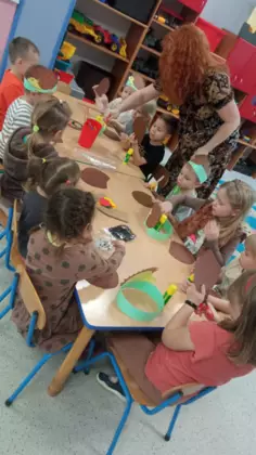 Przedszkolaki siedzą przy stolikach i wykonują z papieru jeżyki.