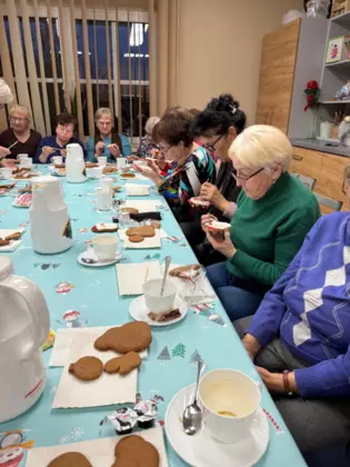 Seniorzy siedzą przy stole i dekorują pierniczki.