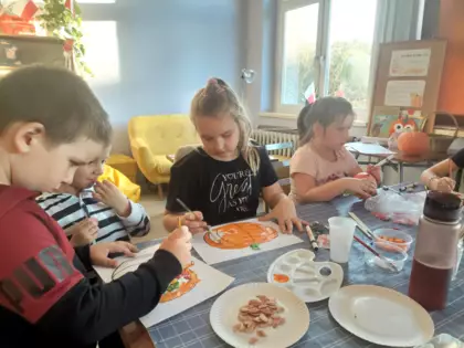 Chłopiec i dziewczynka malują na pomarańczowo szablon dyni.