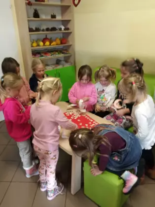 Dzieci przyklejają misia na duże kartonowe serduszko.