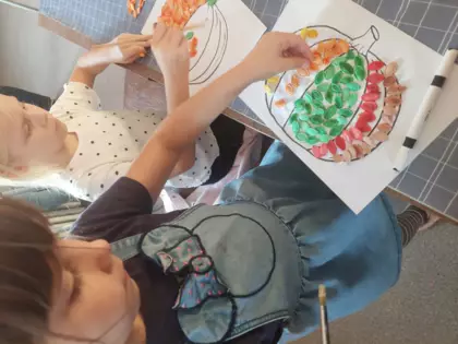 Dziewczynka wykleja szablon dyni - kolorowymi pestakmi dyni.