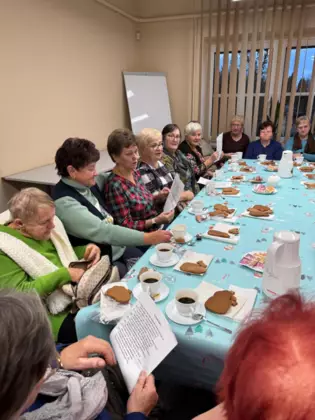 Seniorzy siedzą przy stole i śpiewają piosenki.