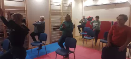 Seniorzy wykonują ćwiczenia relaksacyjne na sali ćwiczeń.