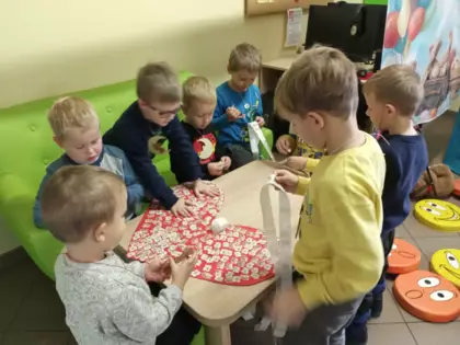 Dzieci przyklejają misia na duże kartonowe serduszko.