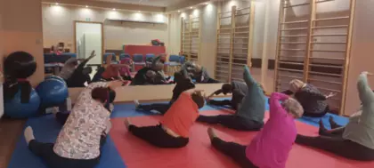 Seniorzy wykonują ćwiczenia relaksacyjne na sali ćwiczeń.