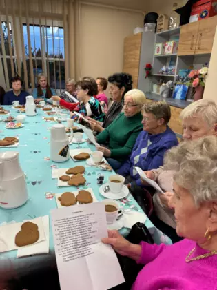 Seniorzy siedzą przy stole i śpiewają piosenki