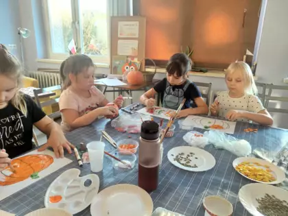 Dziewcyznki wyklejają szablon dyni kolorowymi pestkami dyni.
