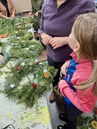 Uczestniczki przy stole dekorują wianki adwentowe.