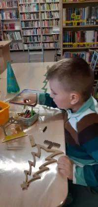 Chłopczyk maluje choinki ze sklejki.