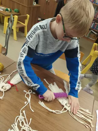 Chłopak wyczesuje wełnę tworząc aniołka z makramy.