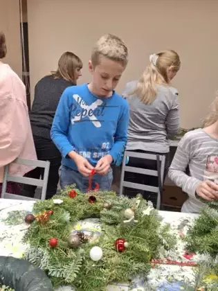 Chłopak wiąże wstążkę na swoim wianku adwentowym.