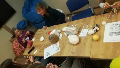 Uczestniczki zajęć siedzą w bibliotece przy stole i szydełkują.