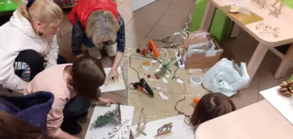 Uczestnicy zajęć w bibliotece i wykonują szopki bożonarodzeniowe.