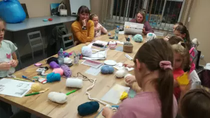Uczestniczki siedzą przy dużym stole w bibliotece i tworzą swoje prace na szydełku.