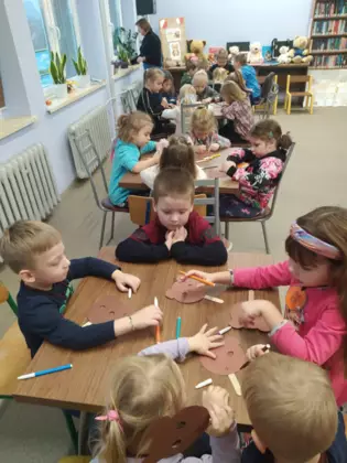 Dzieci siedzą przy stoliku i wykonują prace plastyczne.