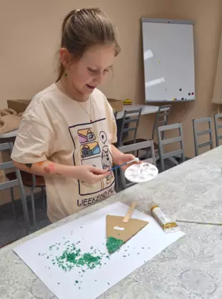 Dziewczynka wykleja choinkę kolorowym ryżem.