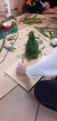 Dzieci przyklejają do makiety świąteczną choinkę z gałązek.
