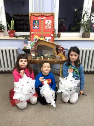 Dzieci przed Stajenką Betlejemską. W rękach trzymają zrobione przez siebie ozdoby świąteczne.