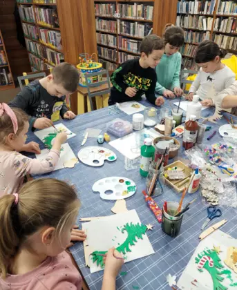 Uczestnicy malują farbkami drewniane choinki.