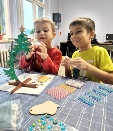 Dwóch chłopców dekoruje drewnianą choinkę.